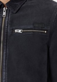 Giacca bomber nera realizzata in tessuto morbido con colletto a coste, dotata di una grande tasca con zip sul petto e di un'etichetta con logo.