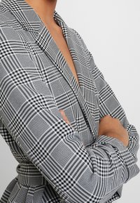 Svart och vit rutad blazer med en strukturerad krage och långa ärmar, med ett hounds-tooth mönster och en skräddarsydd passform.