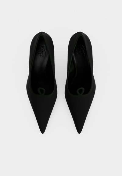 Paire d’escarpins noirs à bout pointu vus de dessus sur un fond blanc uni.