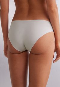Shorty léger en tissu gris clair, présentant une texture lisse, un design taille basse et un dos courbé pour une couverture minimale, avec des bords sans couture.