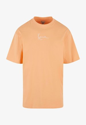 Kerge oranž puuvillane T-särk, ümar krae ja lühikesed varrukad. Ees on valge kalligraafia stiilis tekst "Kane". Sile tekstuur.