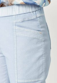 Lichtblauwe broek van een gestructureerde stof; heeft een brede elastische tailleband en meerdere achterzakken met stiksels.