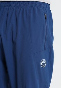 Marineblaue Sporthosen aus leichtem Material, mit elastischem Bund, seitlicher Reißverschlusstasche und einem auf dem Oberschenkel gestickten Logo.