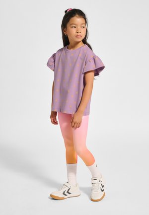 Lilla t-shirt med gule mønstre, korte flæseærmer; kombineret med leggings med gradient fra pink til orange, hvide sneakers og ankelstrømper.