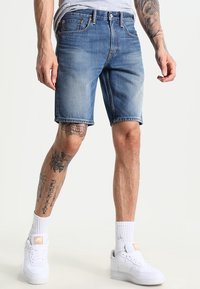 Ljusblå denimshorts med en blekt finish, fem fickor och bälteslatchar. Bärs med vita sneakers och ankelsockor.