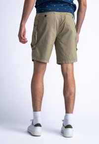 Shorts cargo couleur khaki, arrivant au genou, avec une coupe décontractée, présentant des poches latérales et une texture de tissu uni. Portés avec des chaussures blanches et des chaussettes.