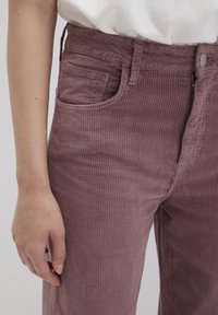 Purple corduroy pants with a textured, ribbed fabric. Features a front pocket and a button closure. The waistband is smooth and fitted.