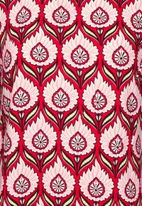 Tejido rojo cubierto con un patrón floral repetitivo; grandes flores blancas con contornos y acentos negros, rodeadas de hojas verdes y destacados amarillos.