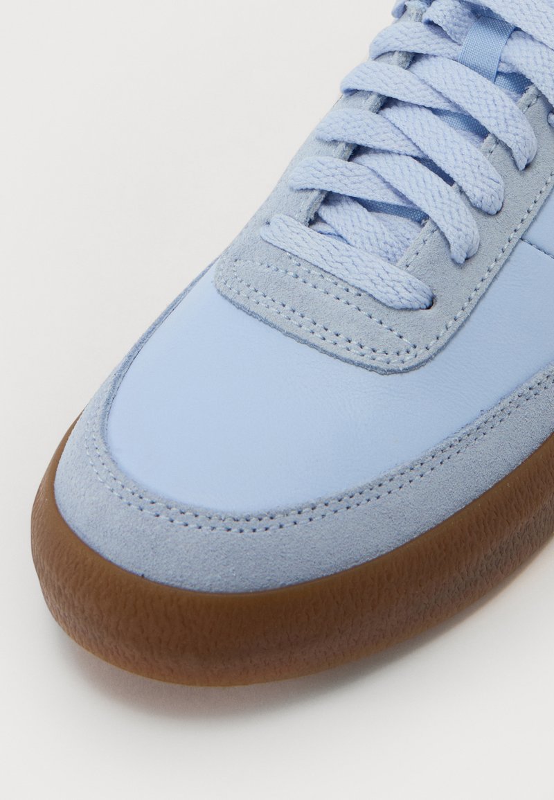 Lichtblauwe sneaker van glad leer en suède materialen. Heeft een ronde neus, een gestructureerde bruine rubberen zool en platte veters.