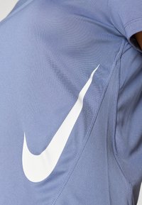 Jasnoniebieska koszulka Nike z krótkim rękawem, z dużym białym logo swoosh po prawej stronie i teksturowaną powierzchnią materiału.