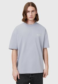 Tricou din bumbac de culoare gri deschis, cu guler rotund și mâneci scurte. Prezintă un logo mic alb pe piept. Material texturat și croială lejeră.