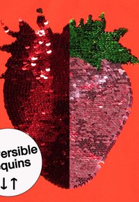 Omvendelig sequin-badge med et halvrødt, halvpink jordbærdesign med grønne accenter, sat mod en lys orange baggrund.