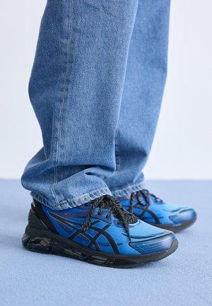 Scarpe da corsa blu con una tomaia testurizzata, dettagli neri e elementi riflettenti. Abbinate a un paio di jeans blu in denim larghi.