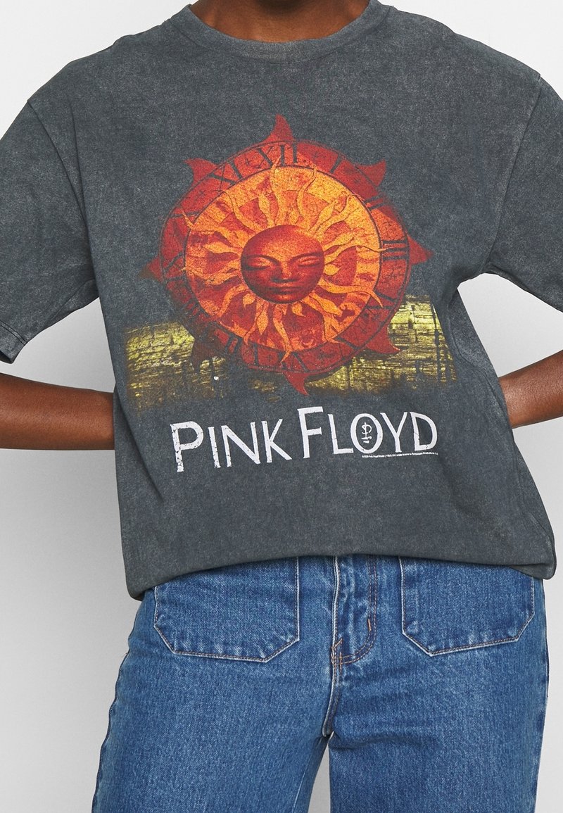 Mörkgrå T-shirt med en soldesign med ansikte och intrikata strålar i orange och gult, samt texten "PINK FLOYD" i vitt.