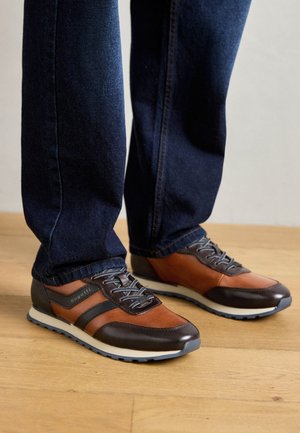 Pruunid ja hallid nahast kingad halli kummitaldaga, dekoratiivse õmblusega ja seotud disainiga, kantud tumedate teksapükstega.