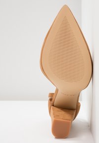 Chaussure en daim beige à bout pointu avec un petit talon bloc, vue de la semelle sur fond blanc.