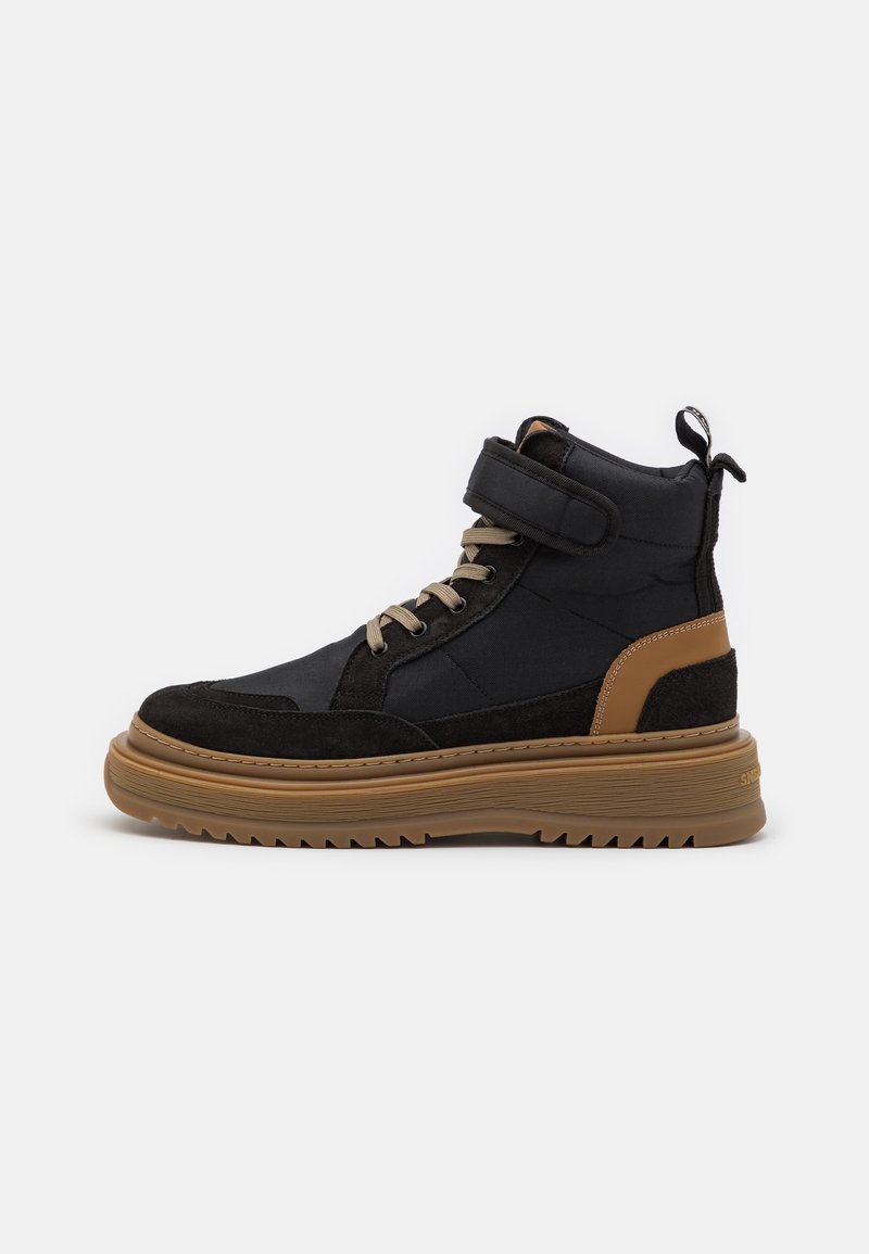 Black and tan high-top sneaker with suede and fabric panels, lace-up design, velcro strap, and rubber sole featuring grooves for traction.