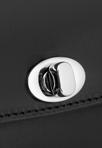 Primer plano de un bolso de cuero negro con un cierre ovalado de plata, textura suave y costuras en contraste a lo largo del borde.