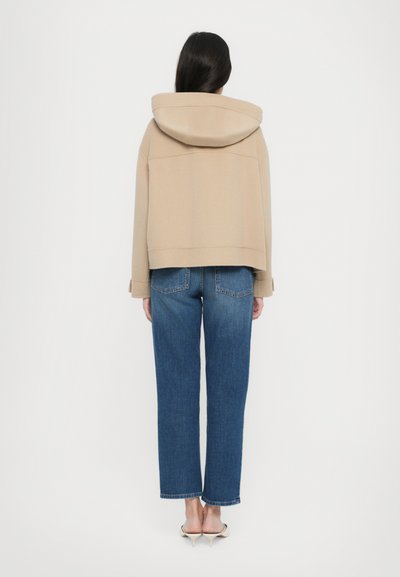Veste à capuche beige au design court, associée à un jean droit bleu avec poches arrière et un ourlet effiloché.