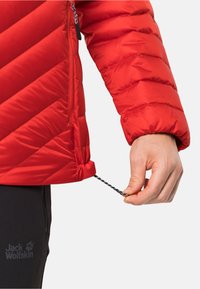Rote Pufferjacke mit diagonaler Steppung, hervorstehendem Reißverschluss und verstellbarem Saumzugband. Hergestellt aus thermischem, wasserabweisendem Material.