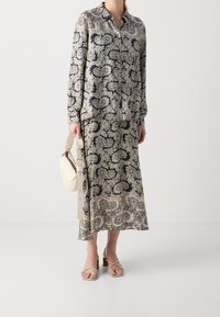 Vestido de manga larga en crema con estampado de paisley en azul marino, con cuello abotonado. Combinado con tacones de tiras beige y un bolso de mano en crema.