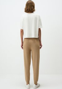T-shirt blanc court associé à un jogger en tricot beige et des baskets blanches. Texture lisse, coupe décontractée, avec des poignets côtelés sur le pantalon.