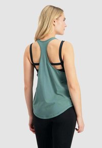 Ärmelloses türkisfarbenes Tanktop mit abgerundetem Saum und Racerback-Design. Sichtbare schwarze Schichtenunterzüge. Glatter, leichter Stoff.