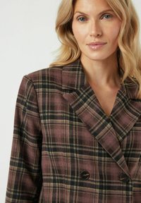 Dubbelgeknoopte geruite blazer in tinten mauve, groen en zwart. Gestructureerde stof met ingezoomde revers en donkere knoopaccenten.