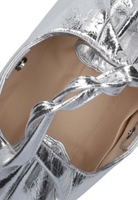 Zilverkleurige metallic handtas met een gestructureerd oppervlak, een gevlochten handvat en een beige interieur met een drukknoopsluiting.