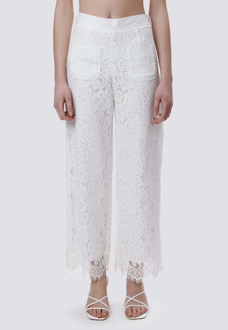 Witte kanten wijde broek met een bloemenpatroon, een soepele tailleband en gegolfde kanten randen. Achterzakken zijn zichtbaar.
