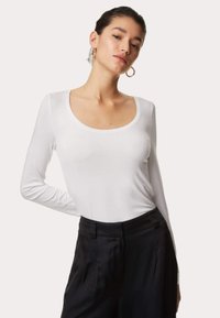Wit long-sleeve top met een ronde hals, gemaakt van zachte stof, gecombineerd met hoog-wijde zwarte broeken met een gladde textuur.