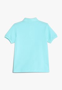 Jasnoniebieska koszulka polo z krótkim rękawem leżąca na płasko, z widokiem na tylną stronę, z ribbowanym kołnierzykiem i mankietami na białym tle.