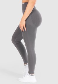 Grijze high-waisted legging gemaakt van rekbaar materiaal, met een geribbelde textuur en een naadloos ontwerp, gecombineerd met witte sportschoenen.