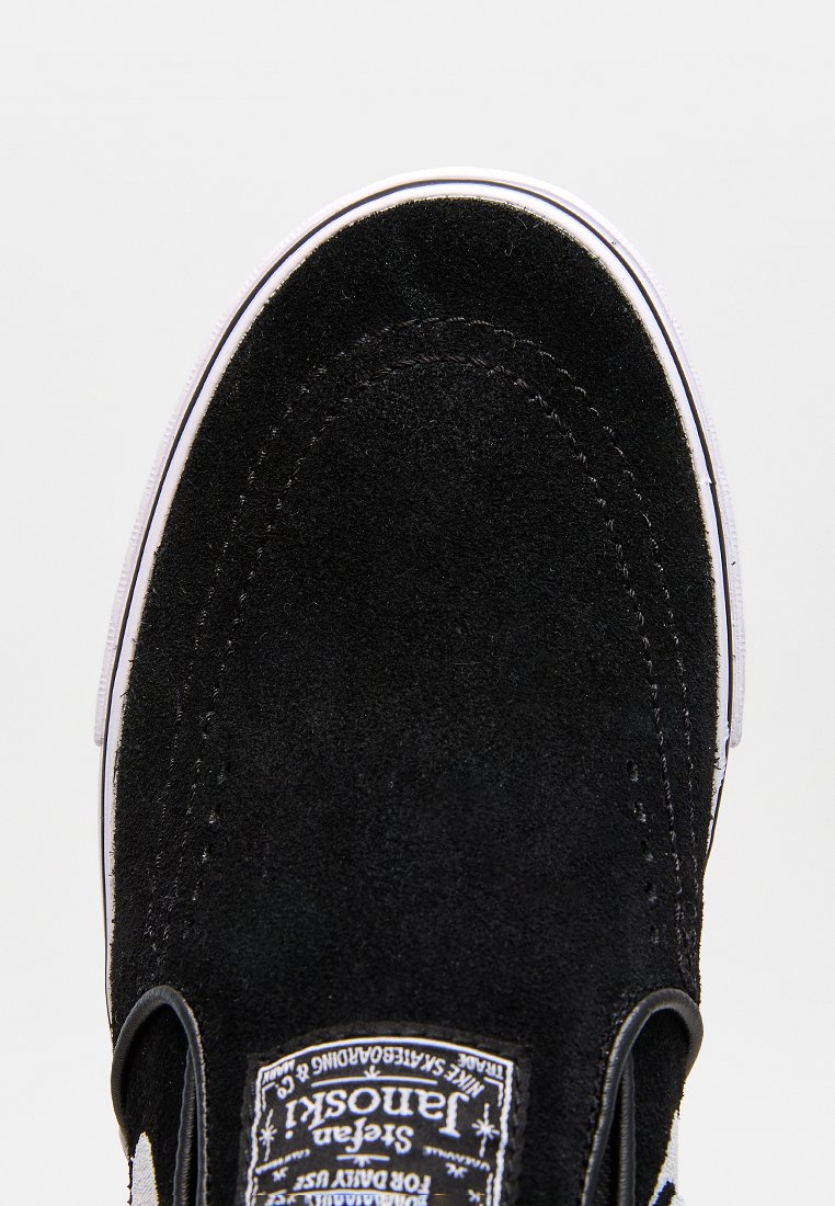 Schwarzer Slipper aus Wildleder mit weißer Gummisohle und Naht. Verfügt über ein Etikett an der Seite. Die Textur ist weich und matt.