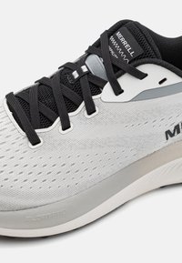 Zapatilla deportiva de color gris claro con parte superior de malla transpirable, puntera reforzada, cordones negros y suela texturizada. Presenta el logotipo en la lengüeta y en el costado.