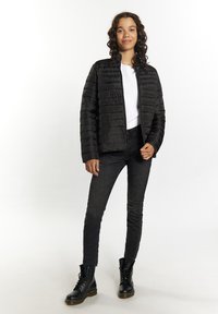 Sort pufferjakke med quiltet design, lange ærmer og lynlås foran. Båret over en hvid tekstureret top og parret med mørke skinny jeans og sorte støvler.