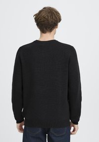 Melnā adīta džemperis ar garām piedurknēm, apaļu kakla izgriezumu un teksturētu audumu; ar ribotiem aprocēm un apakšmalu, nodrošinot ciešu pieguvi.