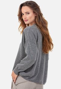 Pull gris en tricot à coupe ample, col rond et épaules tombantes. Texture lisse avec poignets côtelés et légère fente latérale.