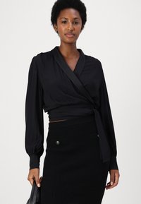 Blusa nera a sirena con maniche lunghe e dettagli in satin sul colletto, abbinata a una gonna a tubino nera a coste con bottoni decorativi.