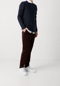 Marinblå kabelstickad tröja, bruna kordflöjlsbyxor och vita sneakers. Tröjan har ribbade ärmslut och nederkant; byxorna har framfickor.