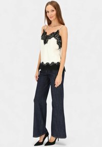 Biała koszulka na ramiączkach z czarną koronkową lamówką, zestawiona z ciemnoniebieskimi szerokimi dżinsami. Modelka ma na sobie czarne buty na wysokim obcasie.