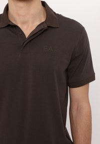 Hnedý polo tričko vyrobené z bavlny, s kontrastným golierom, krátkymi rukávmi a vyrazeným logom EA7 na hrudi.