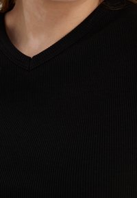 Czarna żebrowana koszulka z dekoltem w kształcie litery V, wykonana z teksturowanej tkaniny, z delikatnym detalem szwów przy dekolcie. Zbliżenie na górną część odzieży.