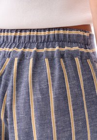 Blauwe gestreepte broeken van een zachte stof. Voorzien van een elastische tailleband en afwisselend gele en witte strepen over de gehele lengte.