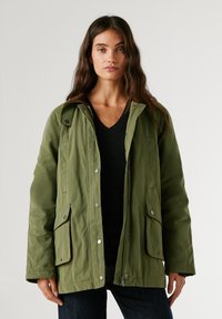 Zaļš parka jaka ar rāvējslēdzēja un pogu aizdari, divi priekšējie kabatas, brūni akcenti uz apkakles un brīva piegriezuma. Tekstūrēta auduma.