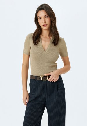 Top corto de color beige con cuello en V y ribetes, combinado con pantalones oscuros de rayas y un cinturón marrón con hebilla dorada.