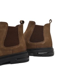 Stivaletti ankle in suede marrone con pannelli laterali elastici, punta arrotondata e suole in gomma nera con dettagli di ammortizzazione ad aria.