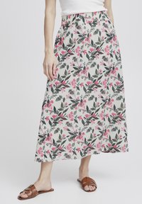 Jupe midi fleuri avec une taille élastique, présentant un fond blanc, un motif floral rose et vert, et des poches latérales. Sandales marron.