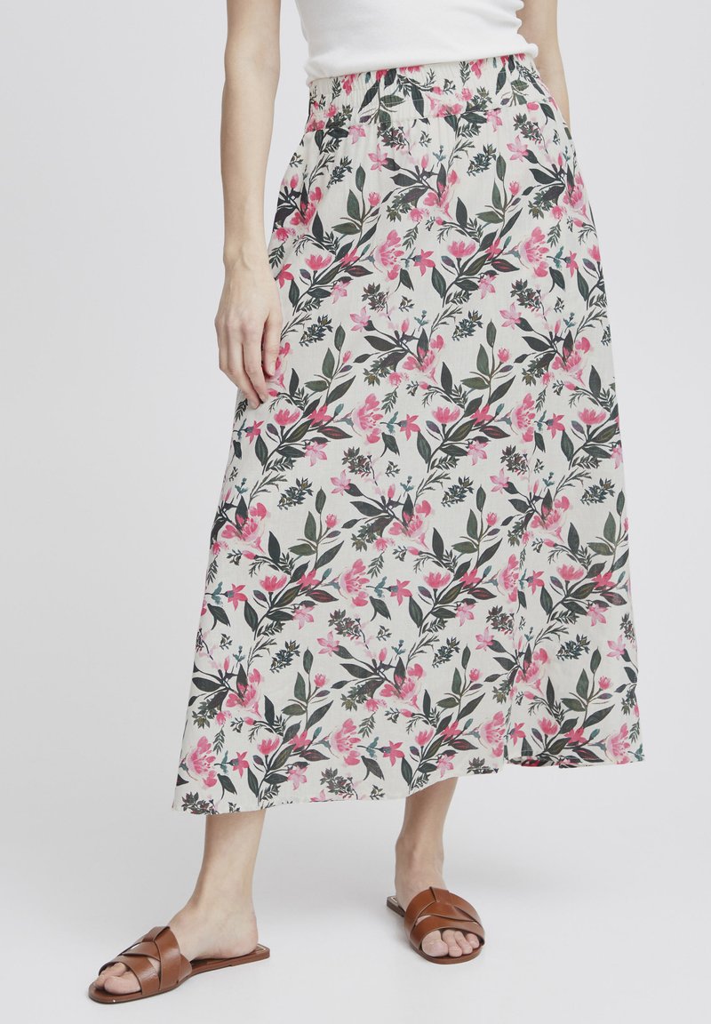 Jupe midi fleuri avec une taille élastique, présentant un fond blanc, un motif floral rose et vert, et des poches latérales. Sandales marron.