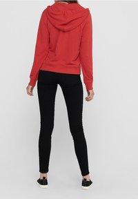 Rode zip-up hoodie met een capuchon, ribgebreide manchetten en zoom. Zwarte slim-fit jeans en zwarte sneakers met een gestructureerd ontwerp maken de outfit compleet.